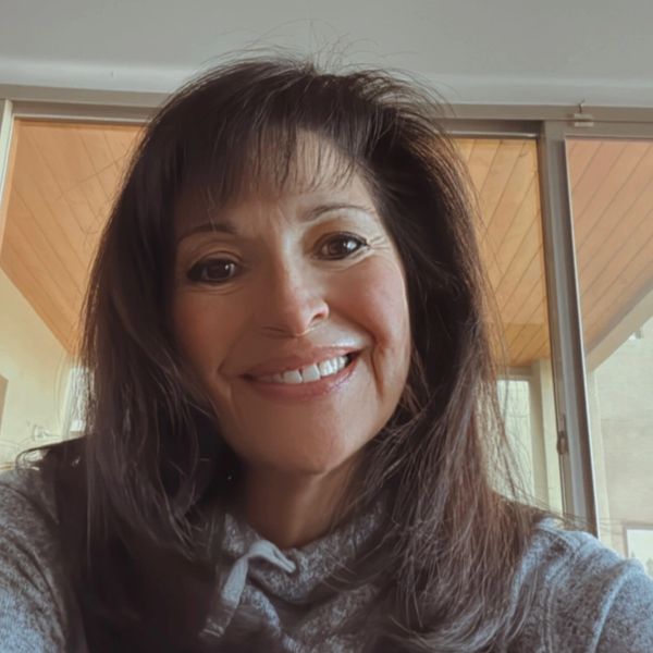 Smiling woman with long brown hair wearing a gray top indoors.