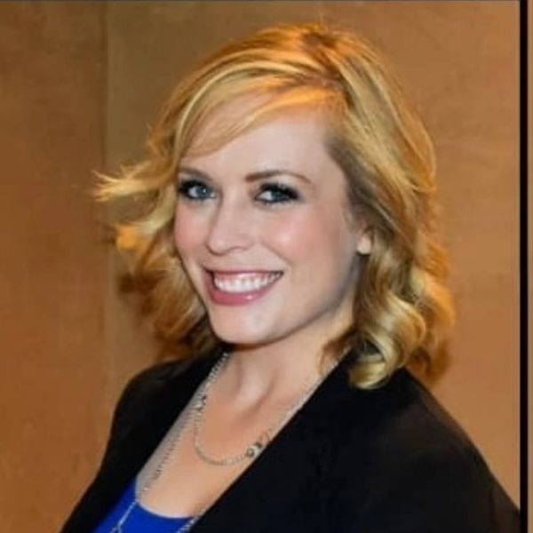 Smiling woman with blonde hair, wearing a blue top and black blazer.