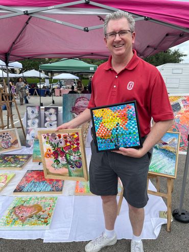 A smiling man holding two pieces of art