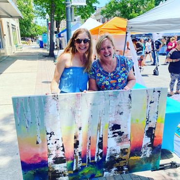 Two women holding a large artwork