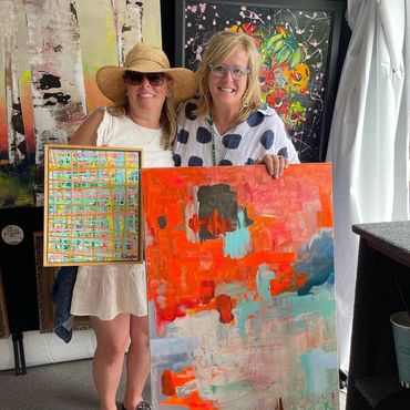 Two smiling women holding artworks