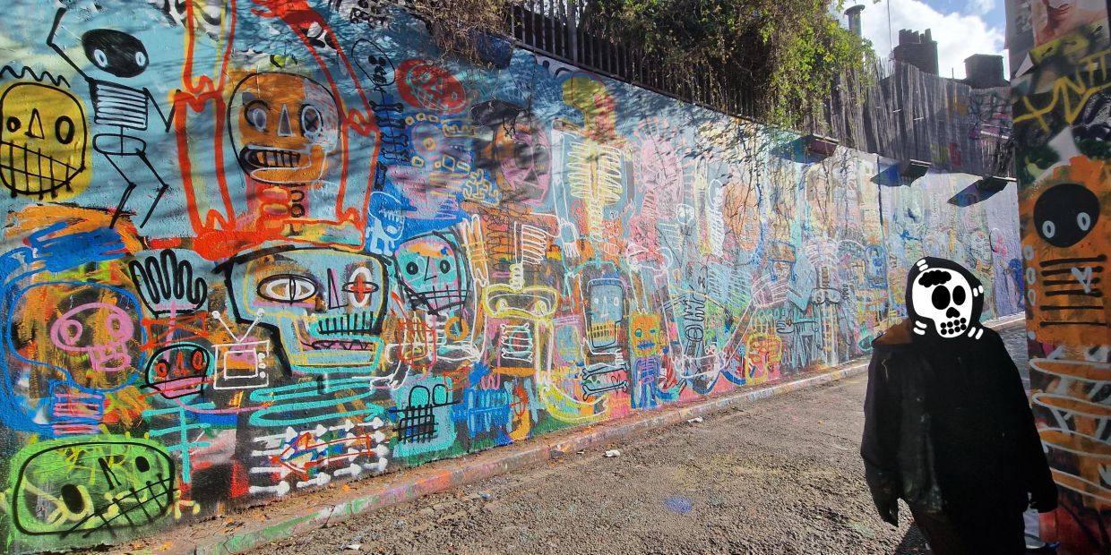 Colorful graffiti wall with skeleton-like faces and a person wearing a skull mask.
