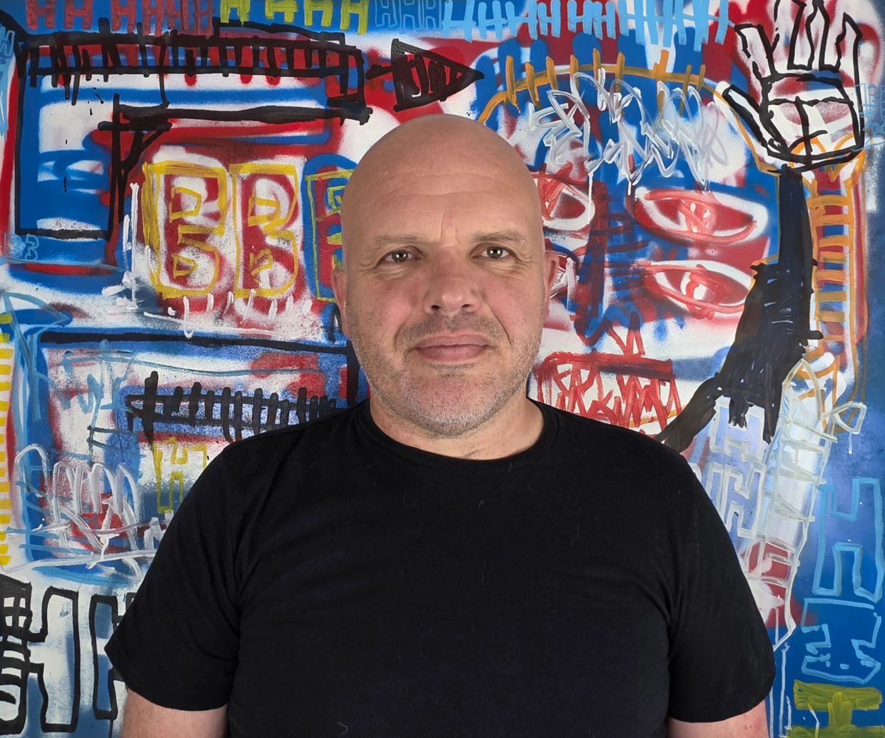 Man in black shirt standing in front of colorful graffiti wall.