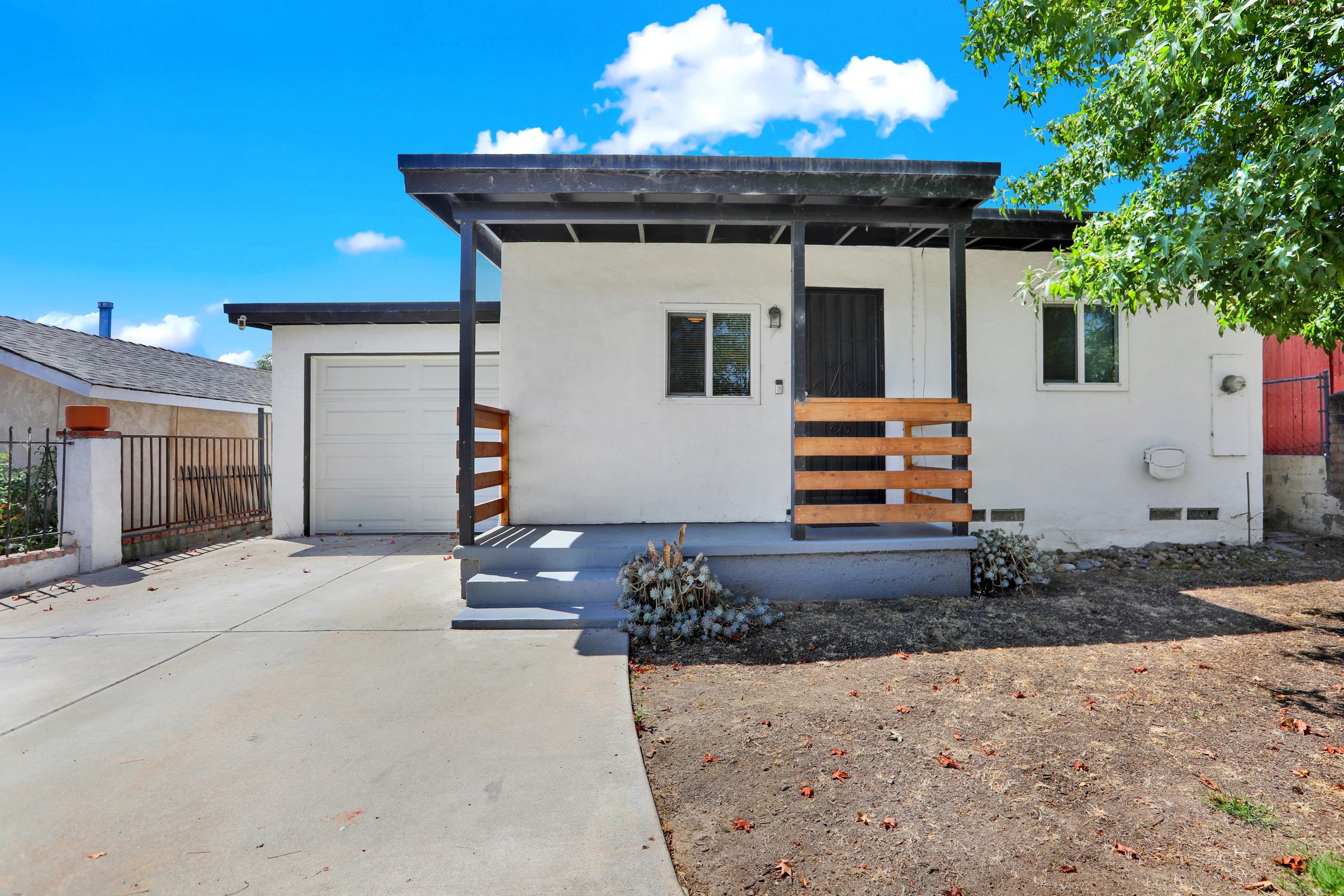 Small white house with a porch and garage under a blue sky.