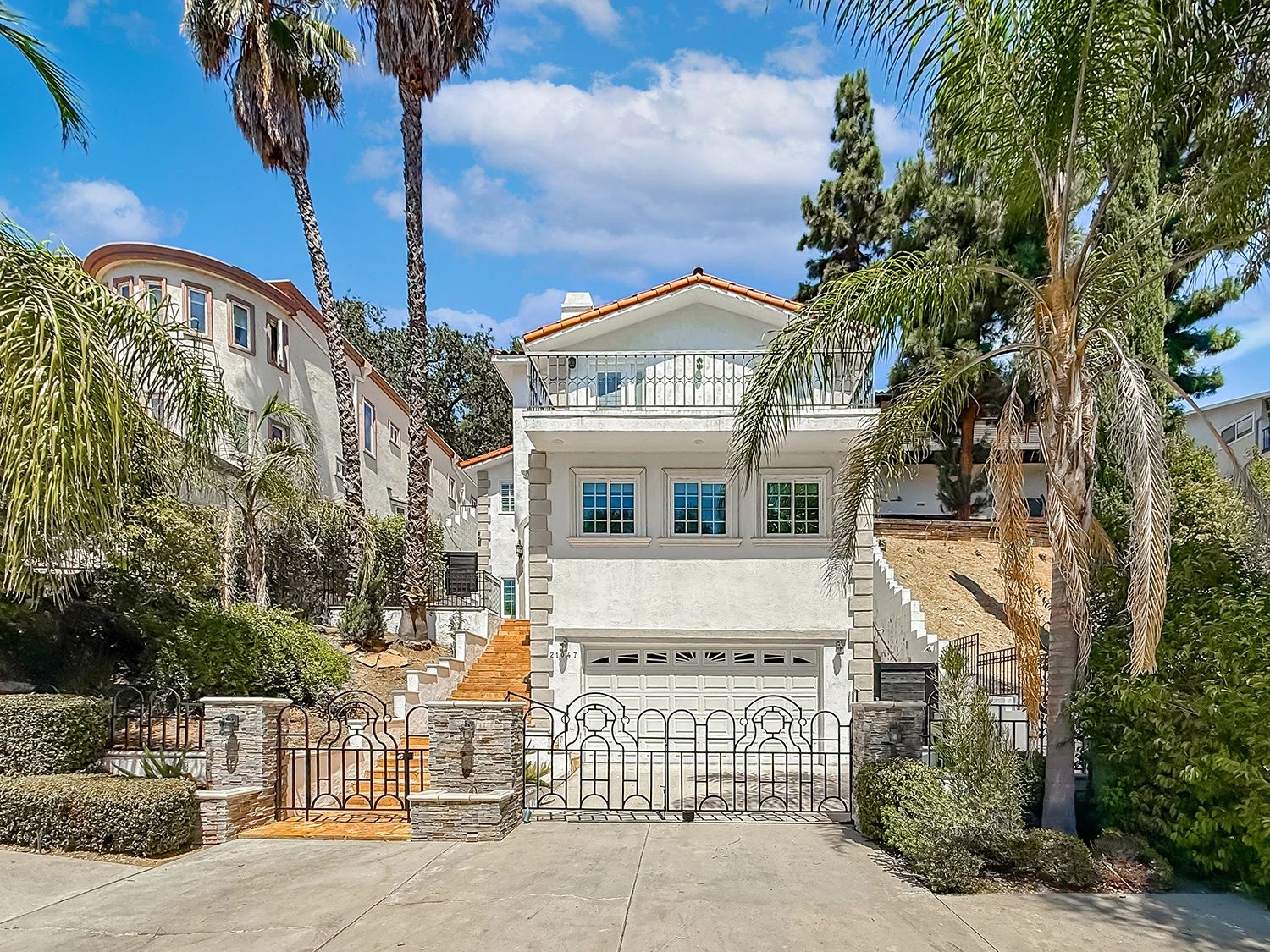 Modern white house with gated driveway and balcony under a blue sky.