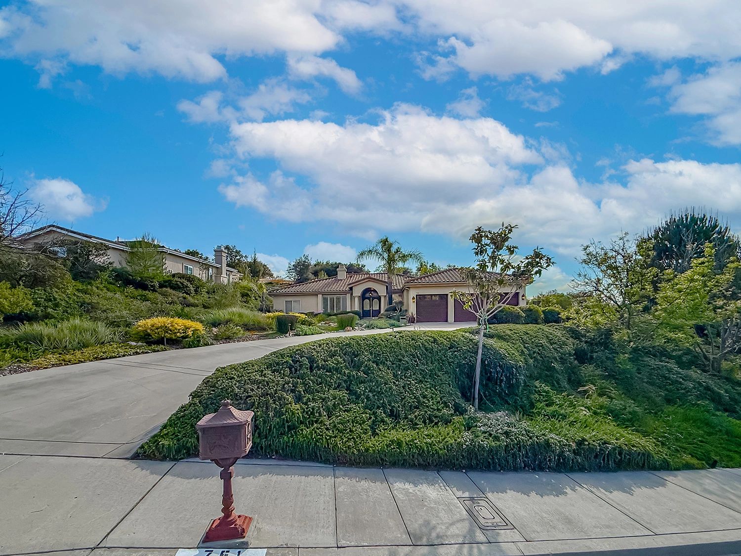 A suburban house with a large driveway and lush greenery under a partly cloudy sky.