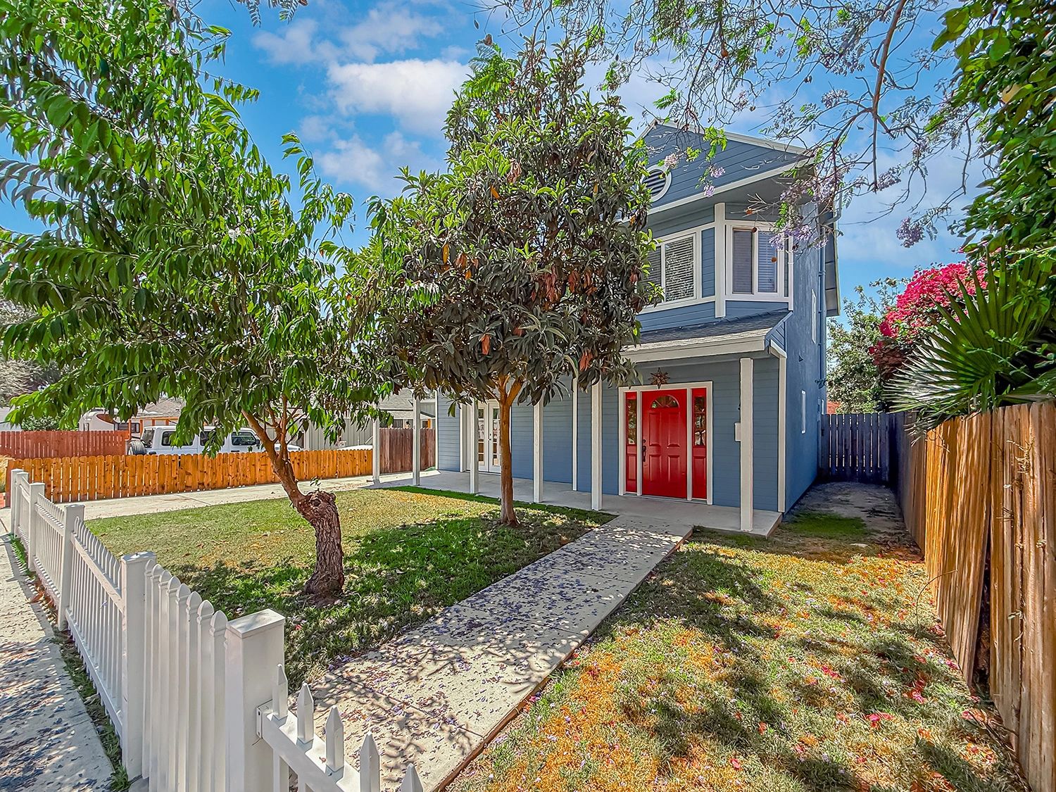 Blue house with red door and fenced front yard.