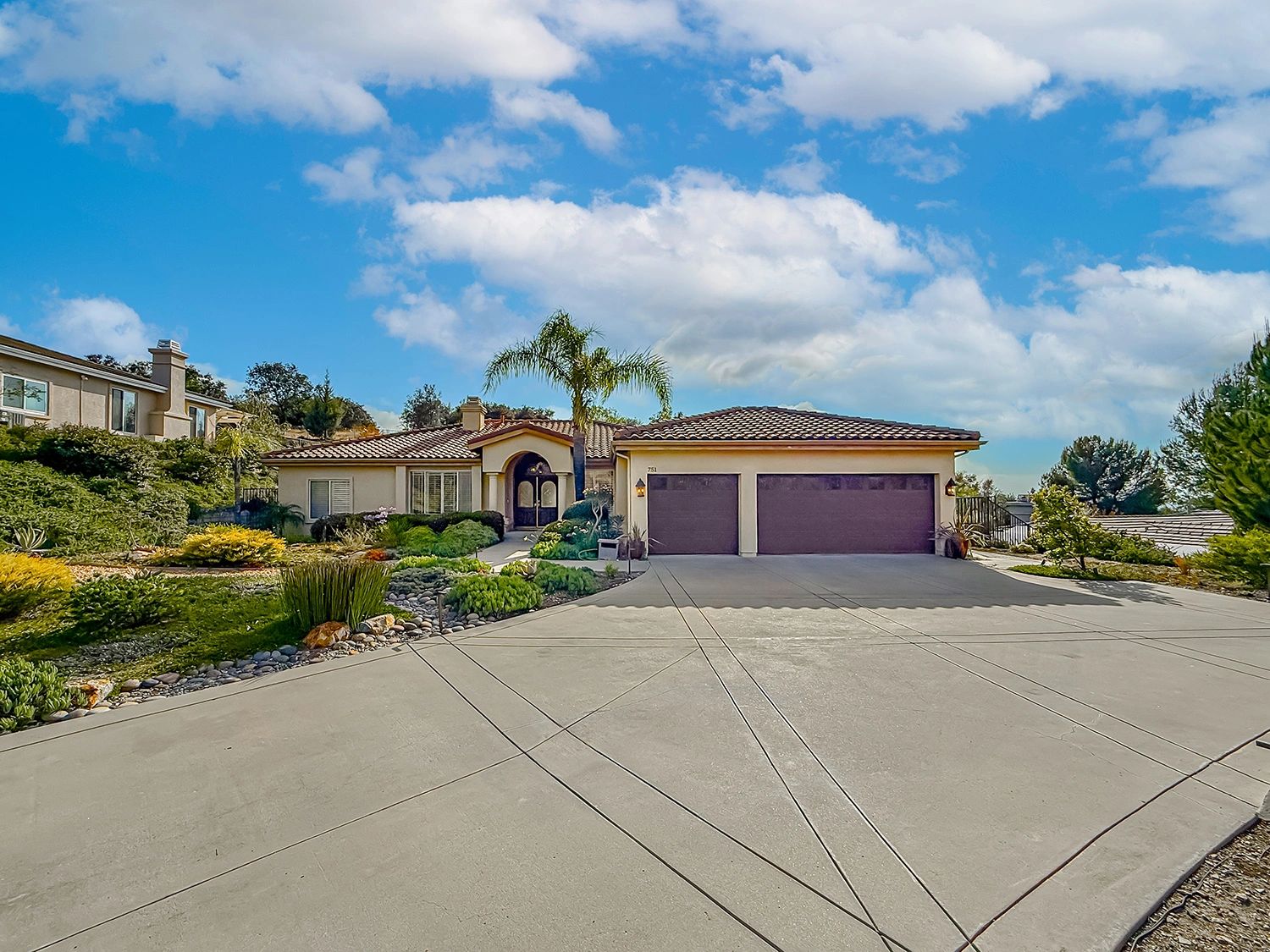 Spacious suburban house with a large driveway and lush landscaping under a bright blue sky.