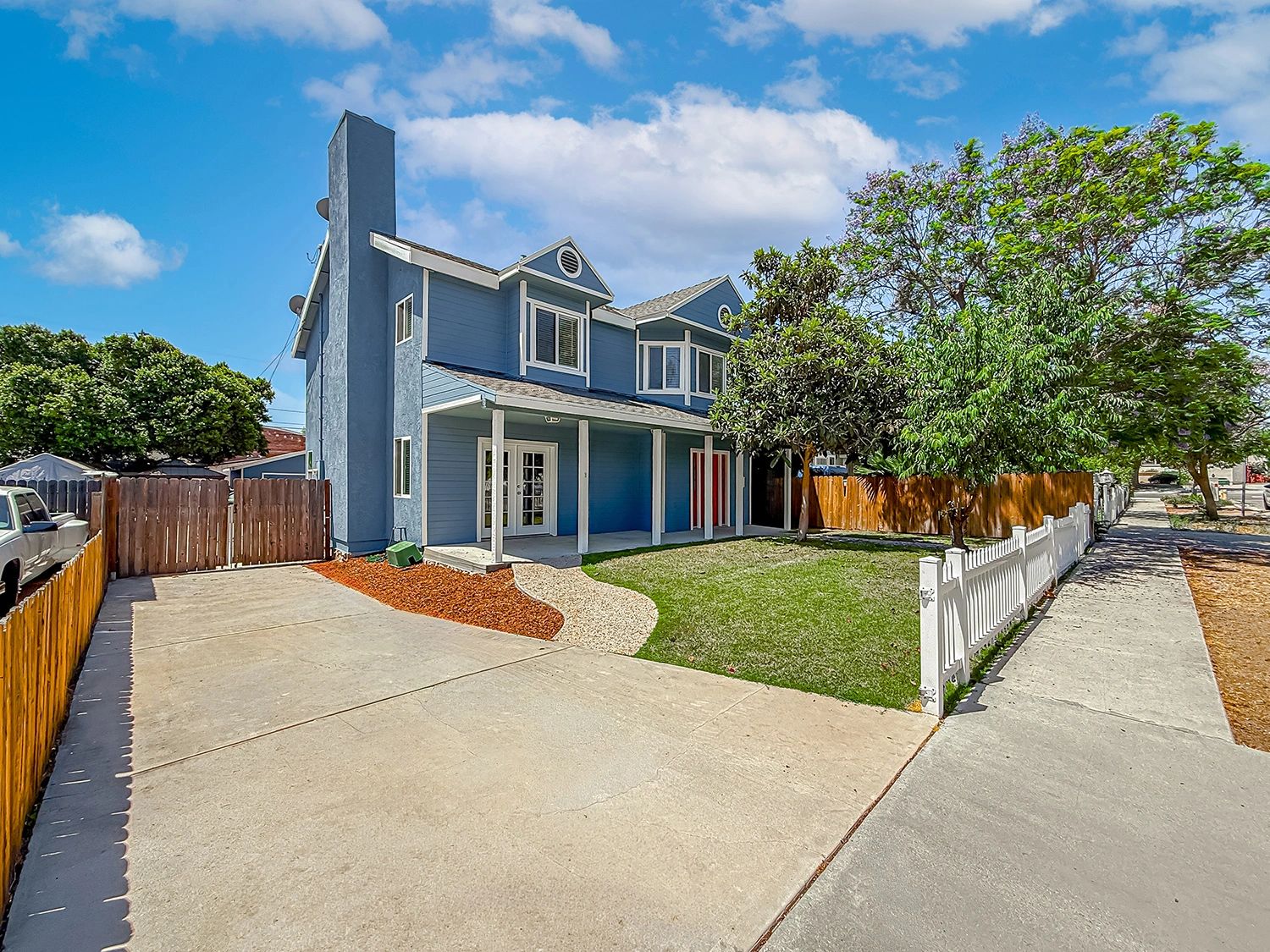 Two-story blue house with driveway and white picket fence.