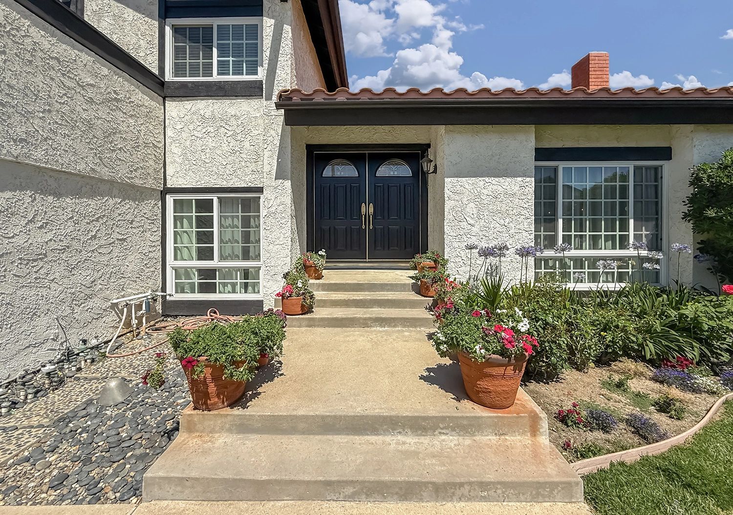 Front entrance of a house with black double doors and flower pots lining the walkway.