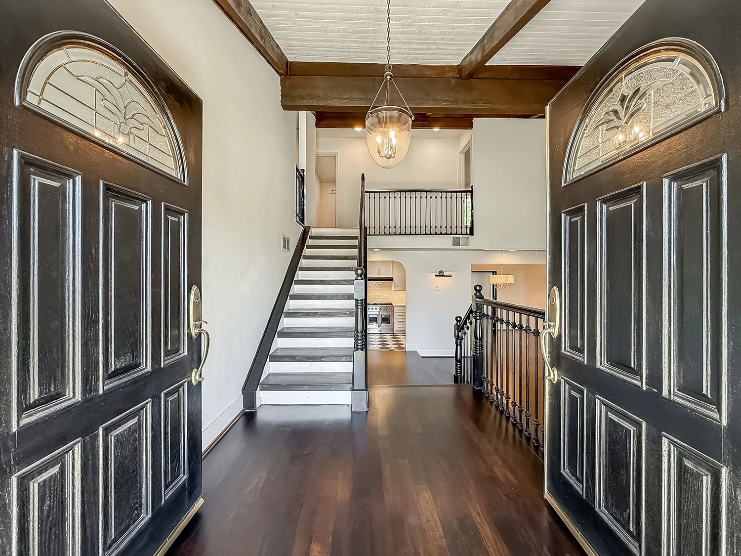Open double doors reveal a staircase and spacious interior with dark wood flooring.
