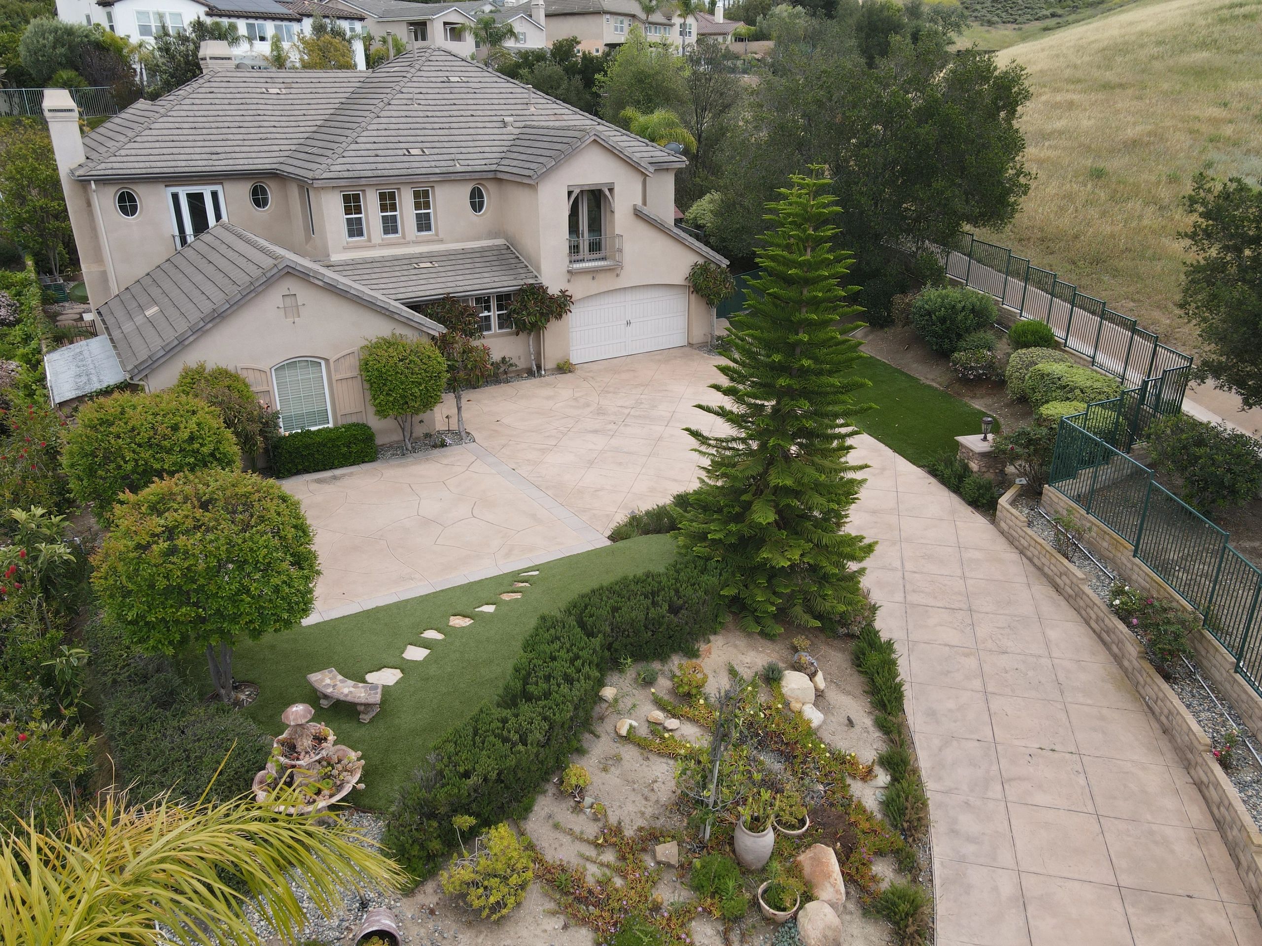 Large beige two-story house with a spacious driveway and lush greenery.