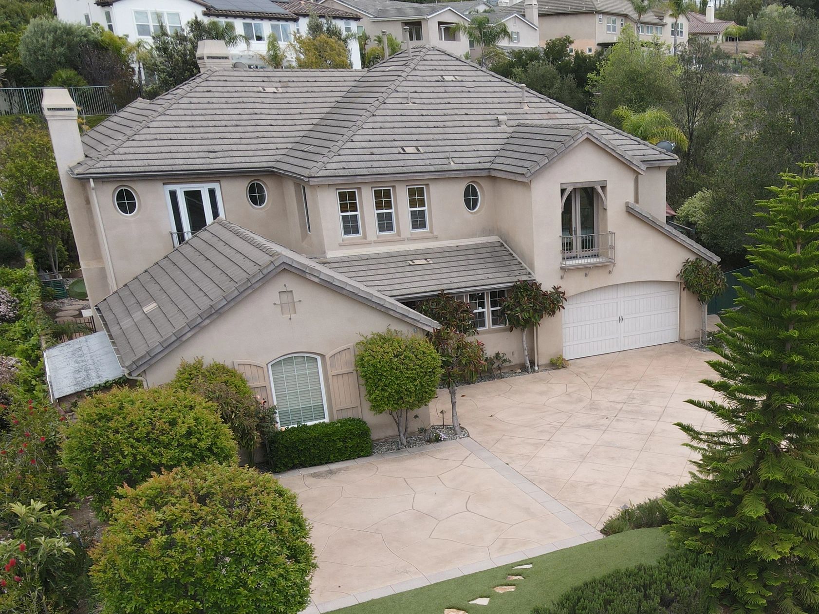 Large beige two-story house with a spacious driveway and lush greenery.
