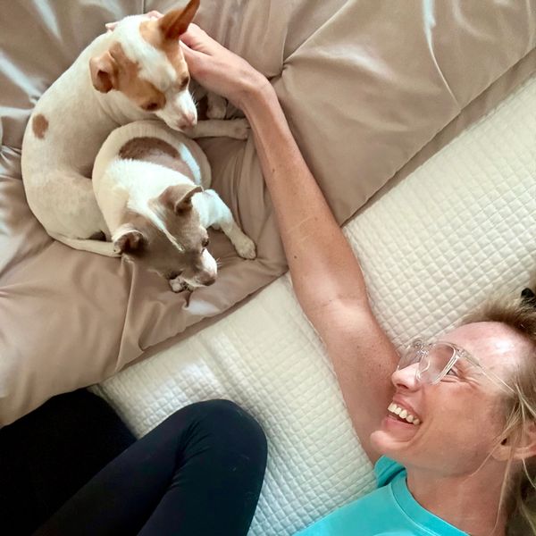 A woman smiles at two small dogs resting on a bed.