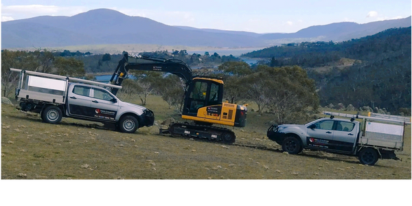 Two utility trucks and an excavator in a scenic, hilly landscape advertising plumbing repairs.