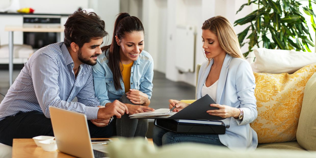 man and woman speaking with a woman who is showing them a contract