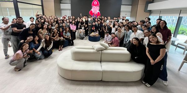Large group photo in modern indoor setting around a white couch.