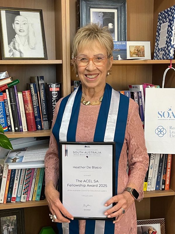 Woman holding an award certificate in front of a bookshelf.