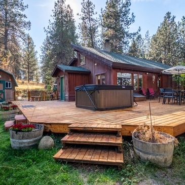 Spacious wooden deck with hot tub beside cabin in forest.