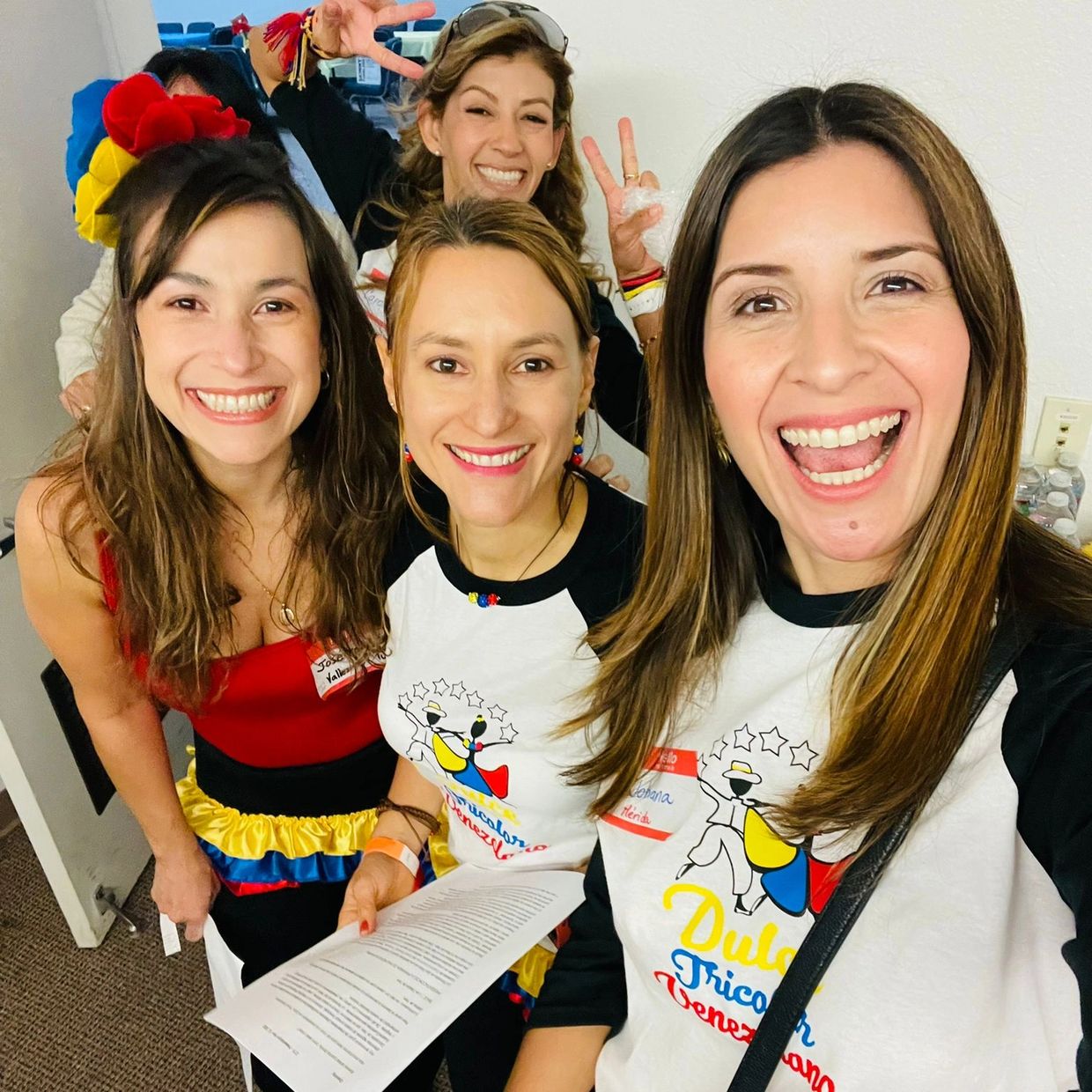 Group of smiling women in colorful outfits and matching shirts posing for a cheerful selfie.