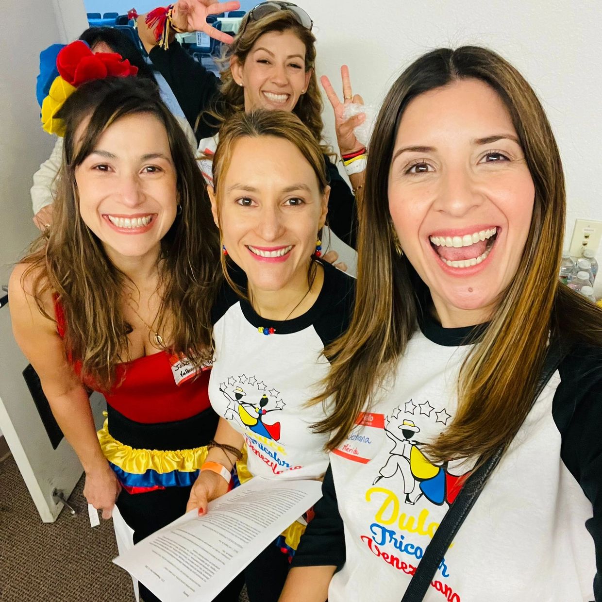Group of smiling women in colorful outfits and matching shirts posing for a cheerful selfie.