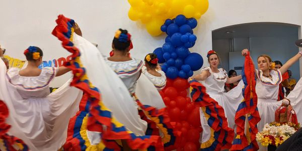 Women dancing in colorful traditional dresses with festive balloon decorations.