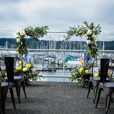 Floral arch installation at Poulsbo Waterfront with marina in the background and colorful florals