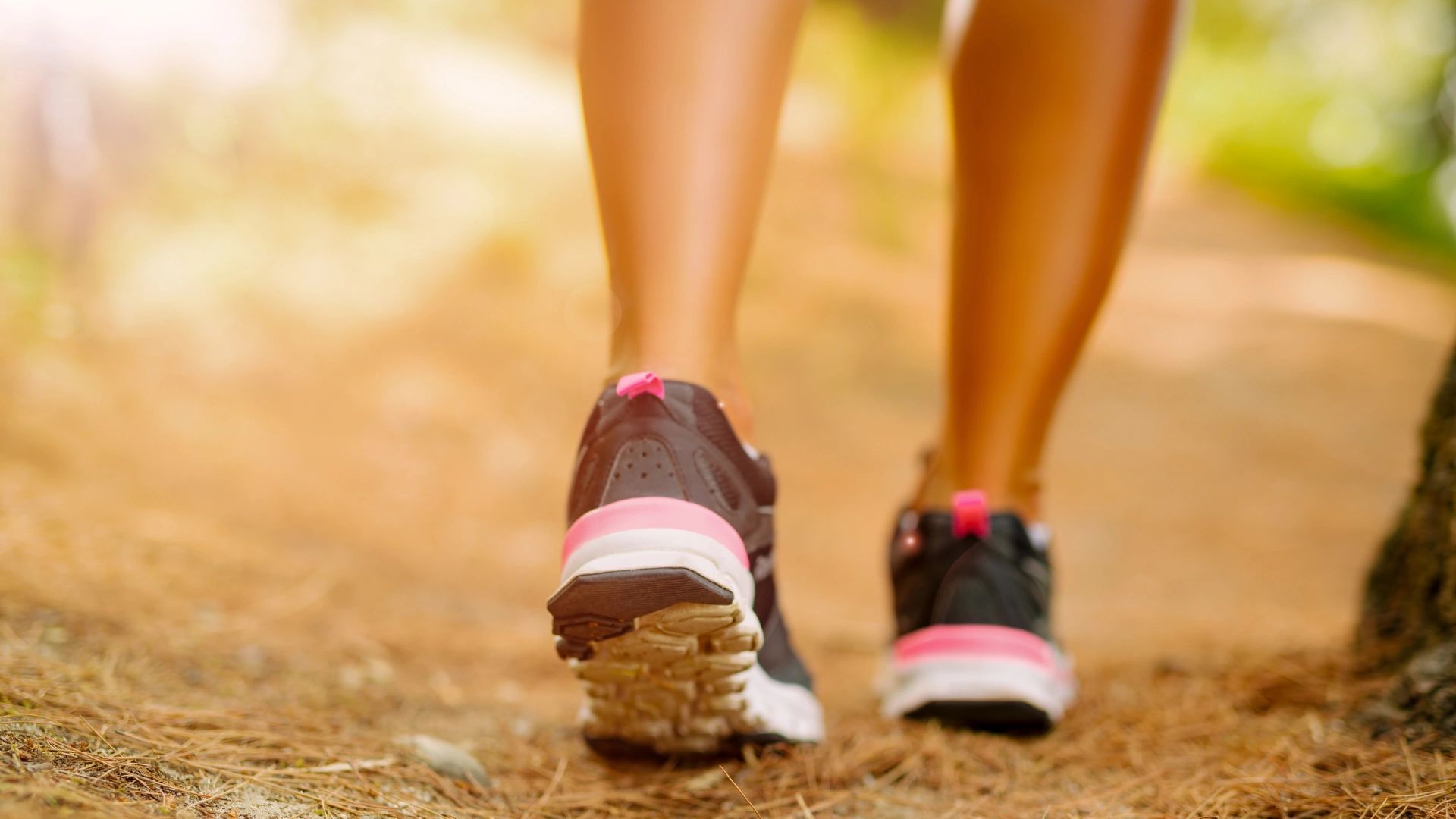 Close-up of person walking outdoors in black and pink sneakers on a dirt path.