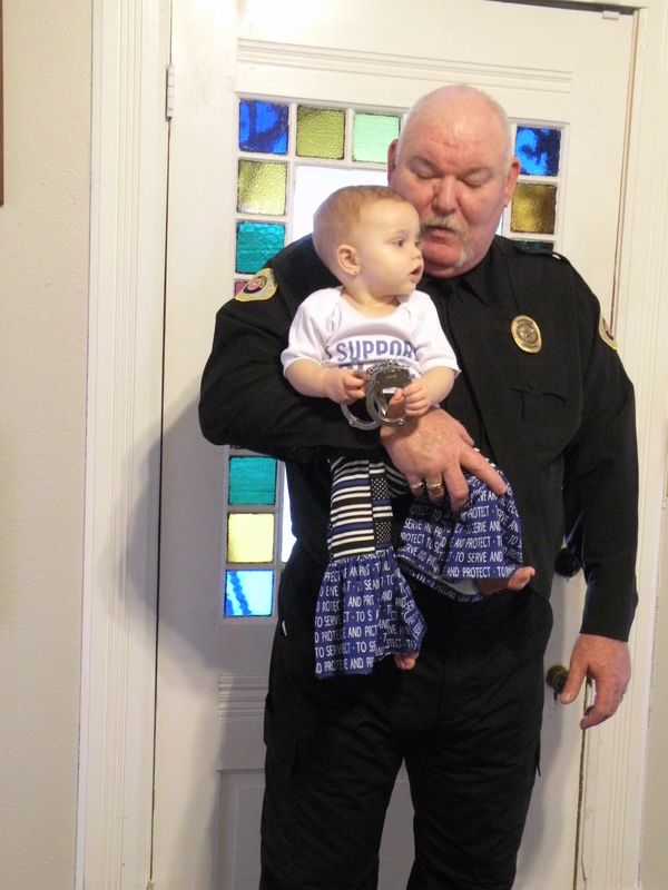 A police officer holding a baby wearing handcuffs and supportive clothing.