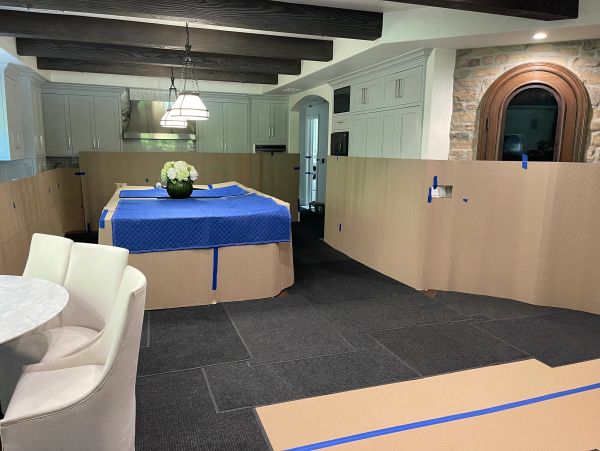 Kitchen area covered with protective cardboard and blue tape during renovation.