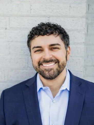 Smiling man with curly hair and beard in a blue suit.