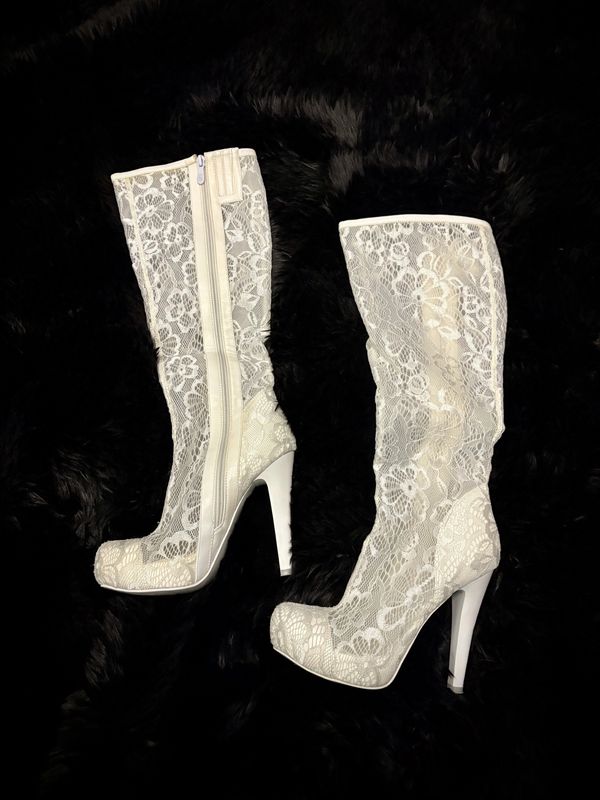 Elegant white lace high-heeled boots with zippers on black background.