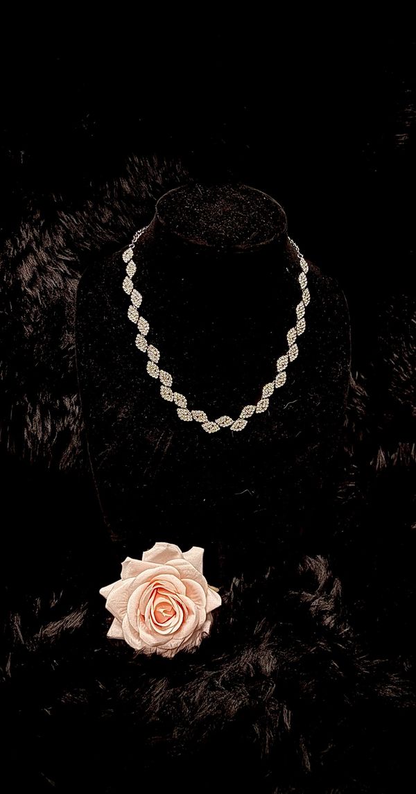Elegant diamond necklace displayed on a black velvet stand with a soft pink rose.