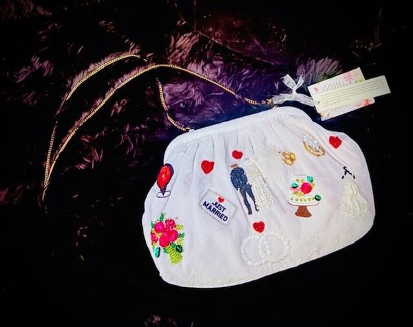 White purse with wedding-themed embroidery and a gold chain on a dark background.