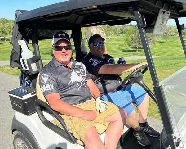 2 men in dark shirts in golf cart