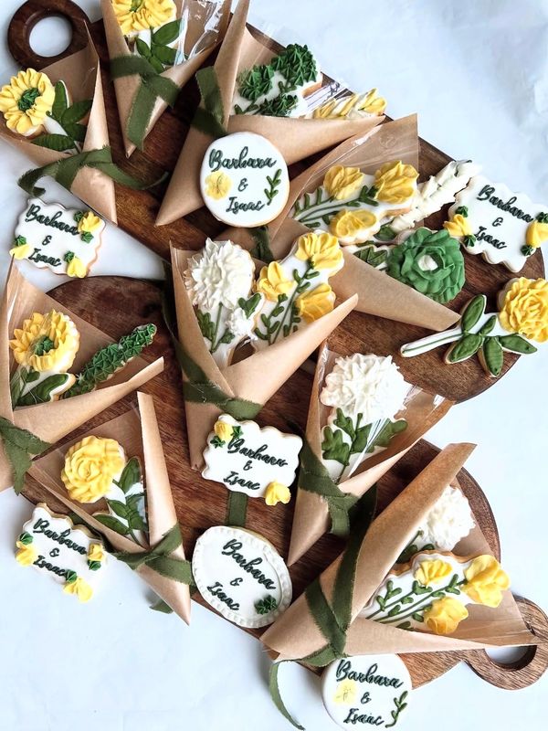 Hand-decorated royal icing cookies with sunflower and floral designs, wrapped in brown paper cones a
