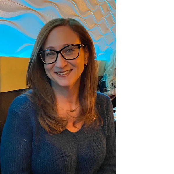 Smiling woman with glasses in a cozy blue sweater at a warmly lit venue.