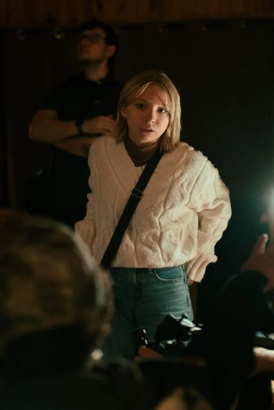Young woman in a white sweater standing, looking thoughtful.