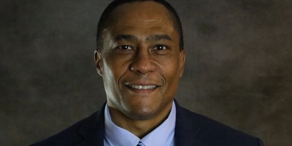 Professional man in suit smiling against a dark background.