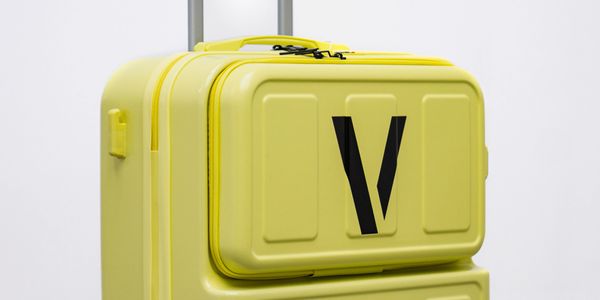 Bright yellow suitcase with black wheels and a bold black 'V' on the front pocket.