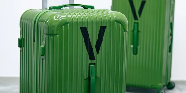 Two green hard-shell suitcases with black V design on wheels on a gray floor.