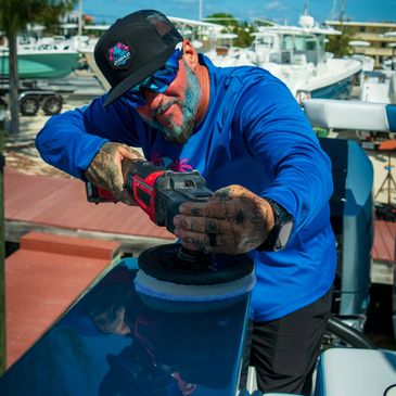 Boat detailer prepping a formula yacht for ceramic coating installation at a marina dock.