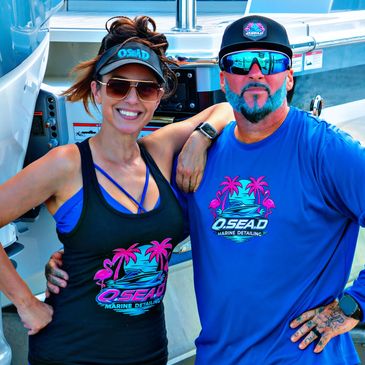 Couple wearing O.Sea.D Islamorada Boat Detailing uniform in front of a yacht docked at marina.