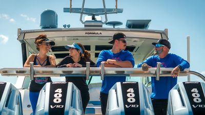 A crew of four boat detailers wearing O.Sea.D uniforms on a large shiny yacht in a marina.