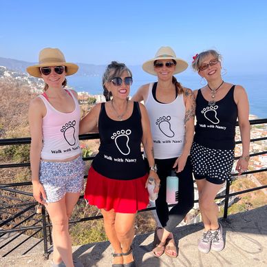 Four women wearing Walk with Nancy shirts posing outdoors with ocean view.