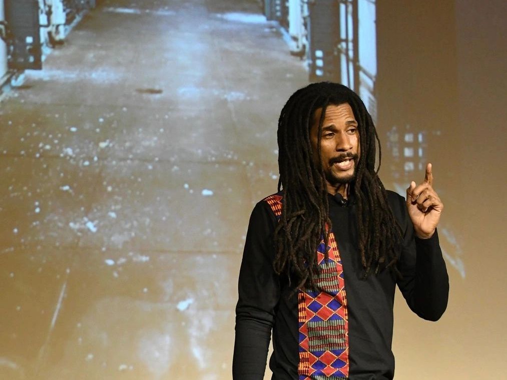Mike Africa, Jr. speaking at an event in front of prison cell photo projection 
