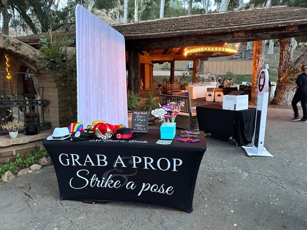 Photo booth prop table with colorful accessories and backdrop outdoors.