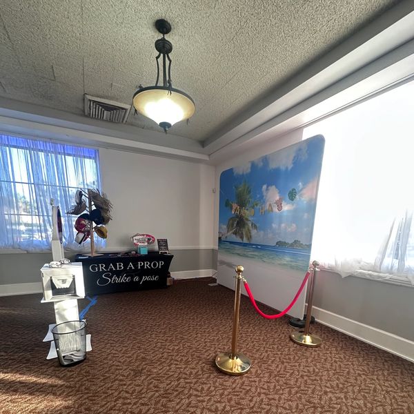 Indoor photo booth setup with tropical beach backdrop and props.