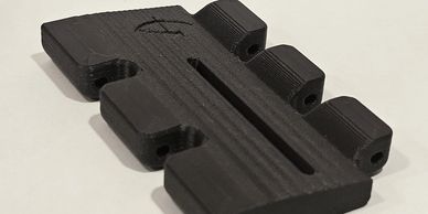 Black 3D-printed object with slots and rounded tabs on a white surface.