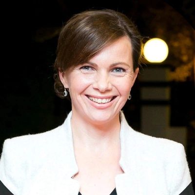 Smiling woman in a white jacket with a dark background and glowing light.
